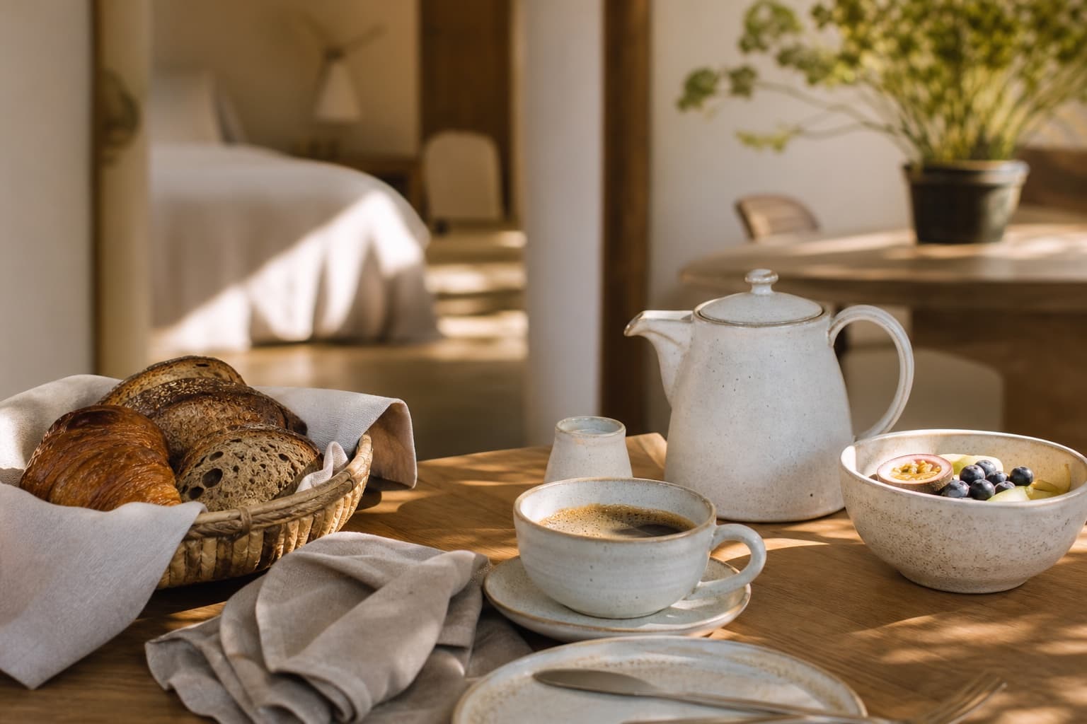 A boutique hotel breakfast setting with coffee, tea, bread, fruit, linen, and ceramic tableware.